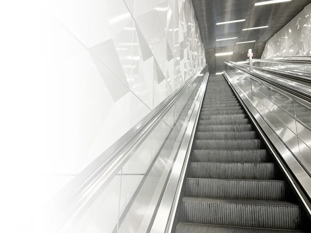 Rolltreppe mit silbernen Handläufen, die nach links ins Weiße ausläuft.
